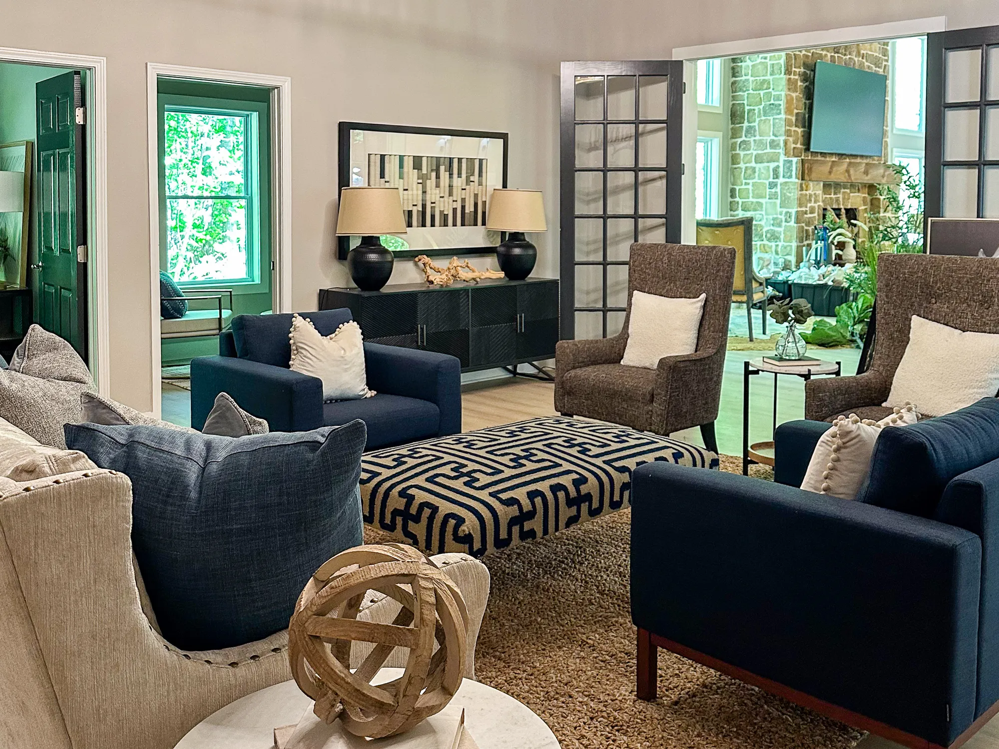 A sitting area with navy chairs, a patterned ottoman, and a stone fireplace beyond