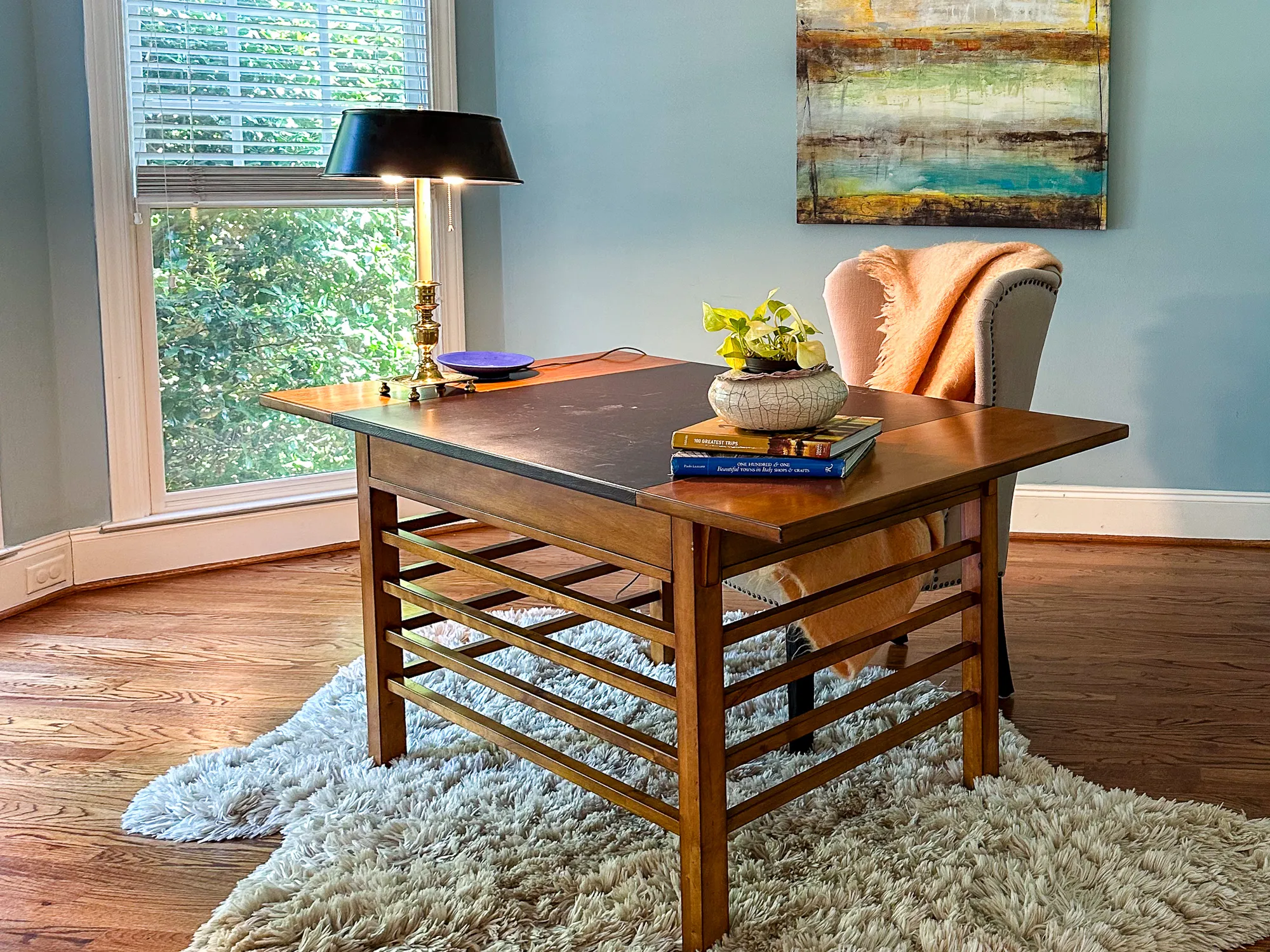 A wood desk with a black lamp and a peach chair on a white rug