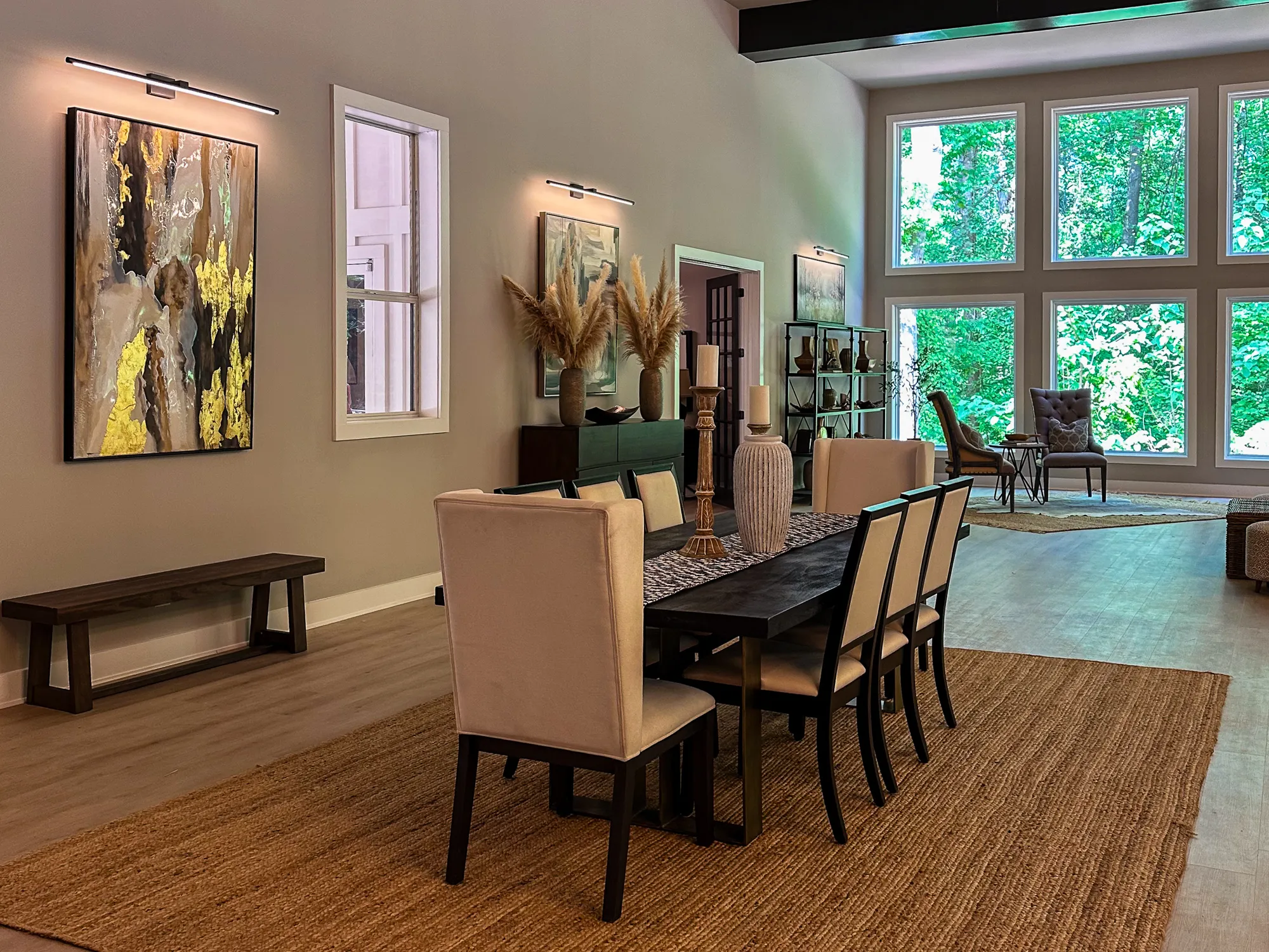 A long dining table with beige chairs, a dark bench, and a wall of windows